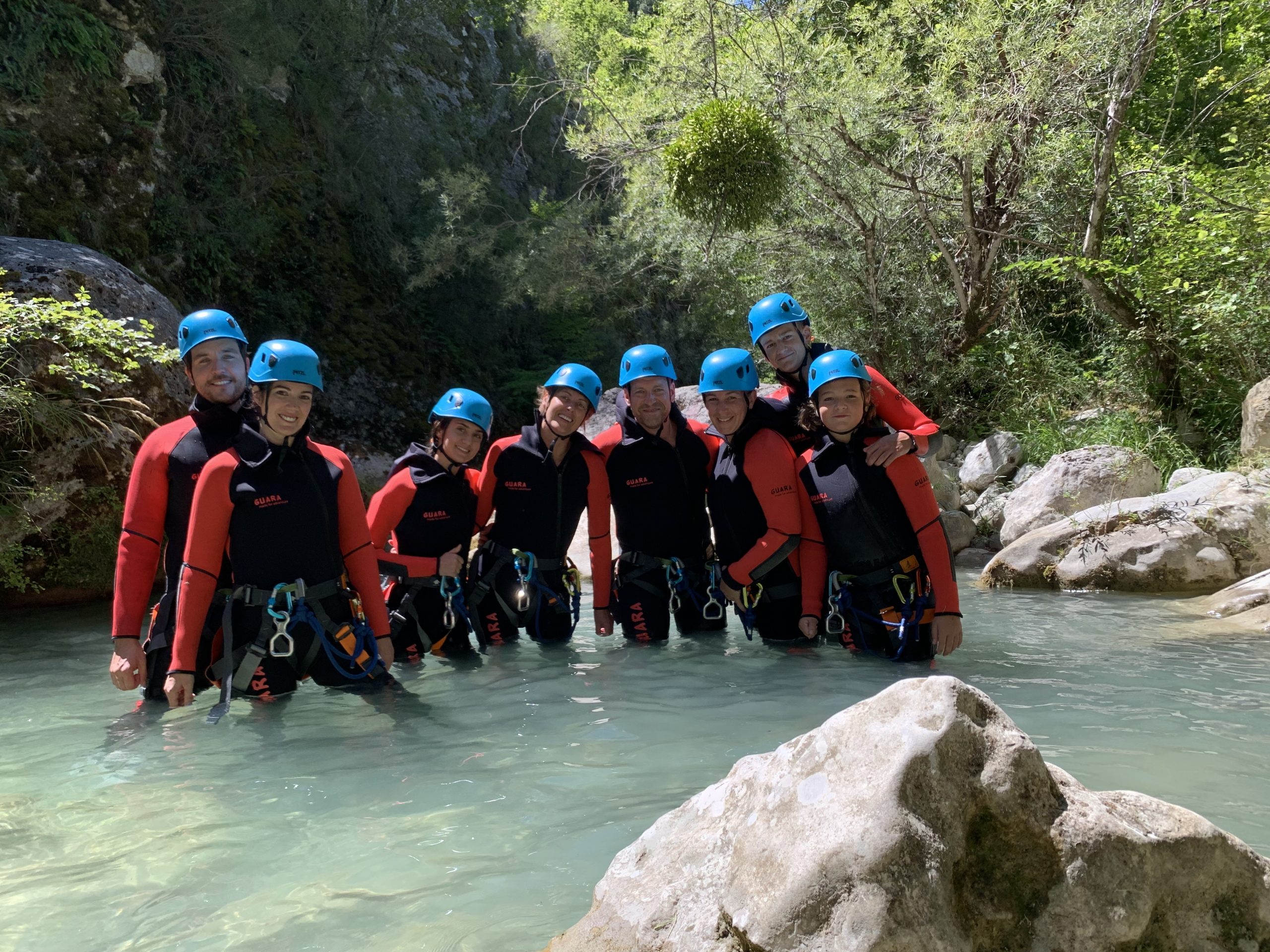 Un groupe d'amis équipé de combinaisons néoprène et de casques bleus pose aligné dans l'eau claire pour un EVG ou EVGF de canyoning