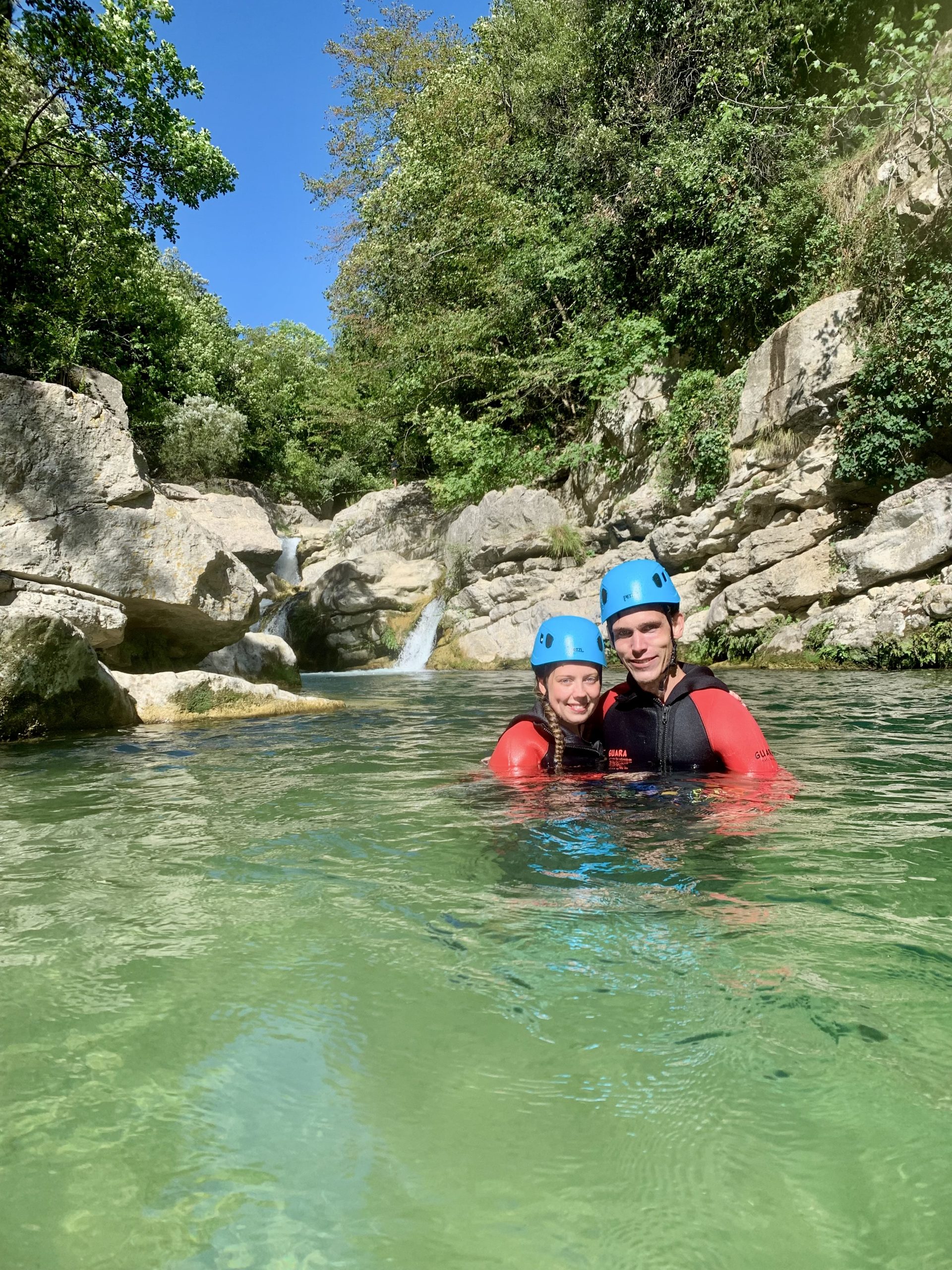 Un couple de participants souriants, immergés jusqu'à la poitrine dans l'eau verte des Gorges du Loup, avec des cascades en arrière-plan.