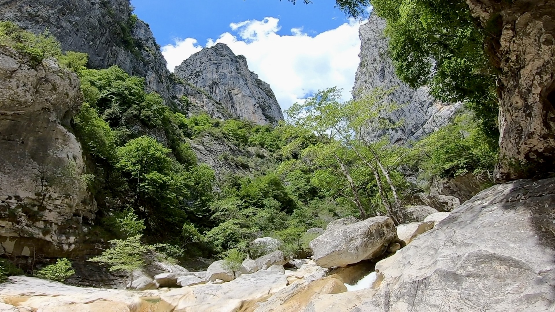 Chaos de gros blocs rocheux et de dalles blanches au milieu d'un grand cirque de falaises calcaires sous un ciel bleu.