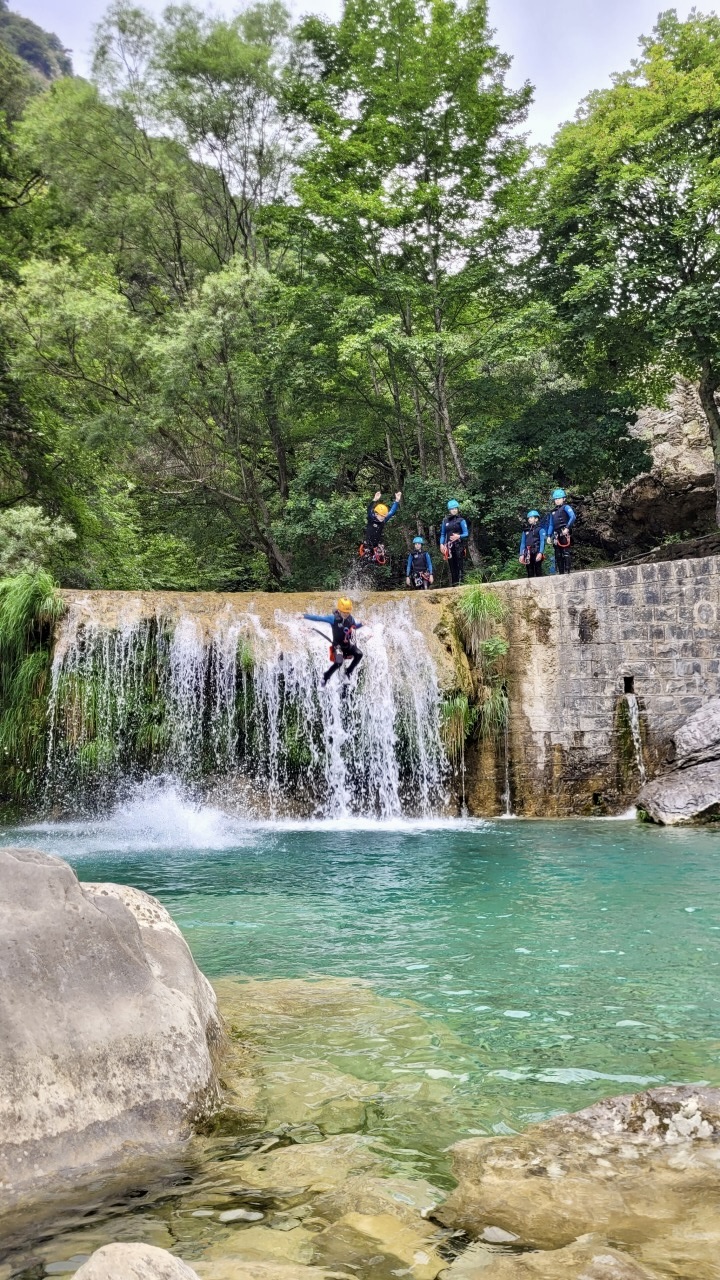 Un aventurier saute du haut d'une falaise calcaire dans une vasque d'eau profonde et translucide au canyon de la Barbaira.
